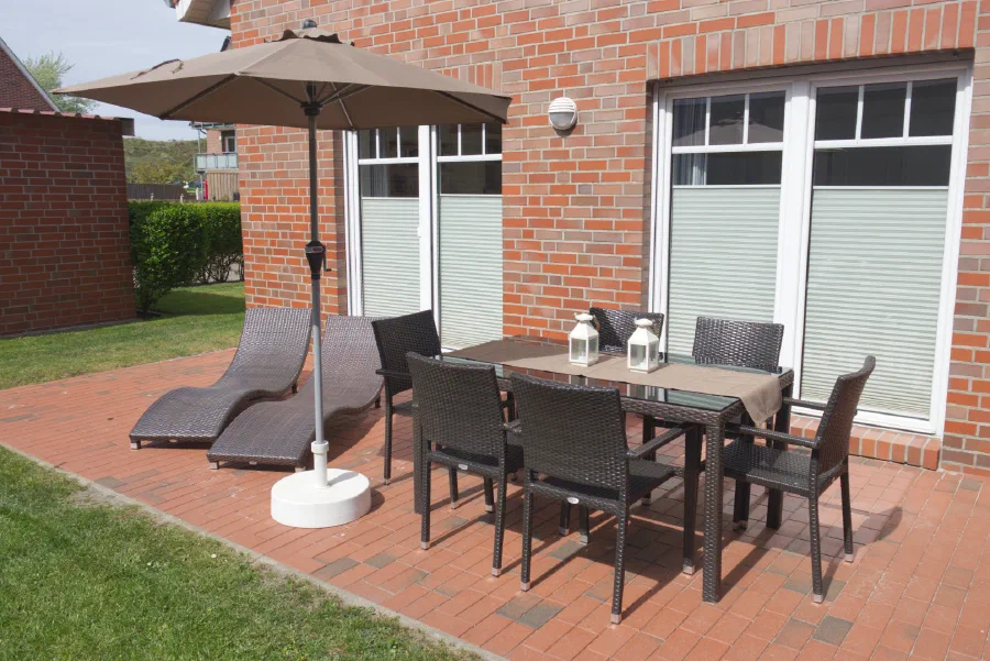 Terrasse mit Gartenmöbeln, Sonnenschirm und Liegen.
